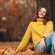 Beautiful girl at autumn park sitting near a tree with falling yellow foliage leaves. Woman smile - PhotoDune Item for Sale