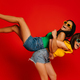 Two playful young women piggybacking each other while having fun against red background together - PhotoDune Item for Sale