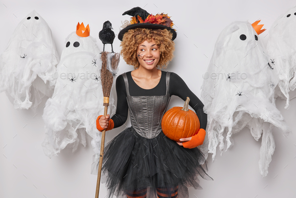 Indoor photo of young pretty happy smiling African american woman in costume of witch holding broom - Stock Photo - Images