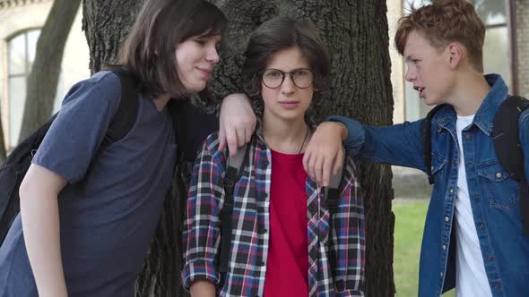 Classmates Teasing Nerd Caucasian Boy on Schoolyard. Portrait of Brunette Scared Schoolboy in alt