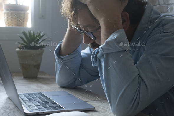 Worried and desperate stressed worker an at the desk holding his head with exhausted expression
