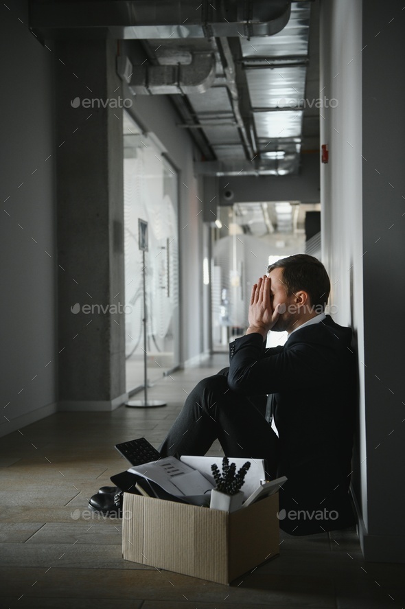 Sad fired businessman sitting outside meeting room after being dismissed.