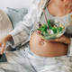 An unrecognizable pregnant woman eats a healthy fresh salad and communicates online on the phone. - PhotoDune Item for Sale