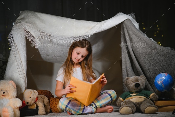 A pretty little girl reading a book on the floor under the lamp. Children and education