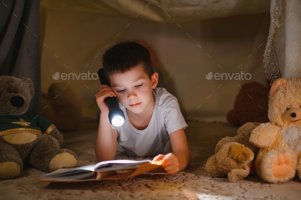 Two little child play at home in the evening to build a camping tent to read books with a flashlight