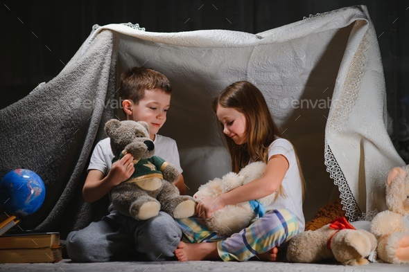 Two child play at home in the evening to build a camping tent to read books with a flashlight