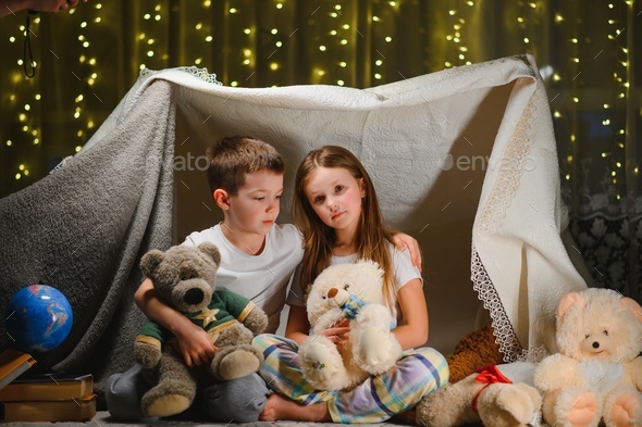 Two children play at home in the evening to build a camping tent to read books with a flashlight