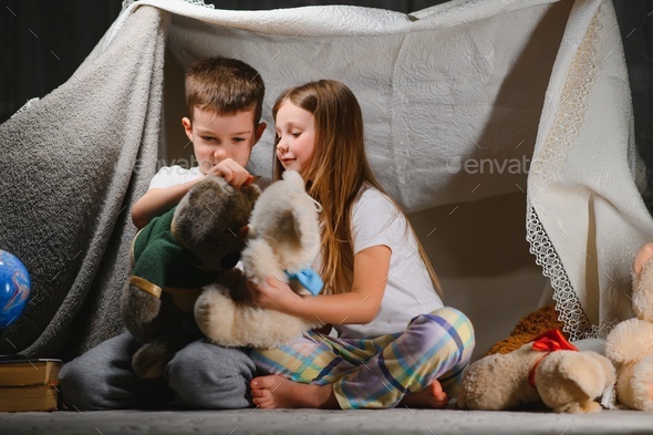 Two child play at home in the evening to build a camping tent to read books with a flashlight