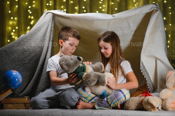 Two children play at home in the evening to build a camping tent to read books with a flashlight