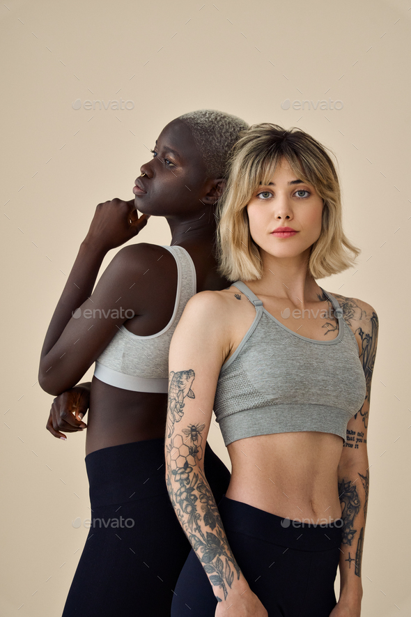 Two cool Black and Caucsian fit girls wearing sport tops vertical portrait.  Stock Photo by insta_photos