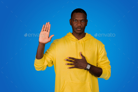 Serious confident strict young black guy presses hand to chest, swears, by his chest