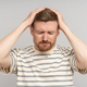 Puzzled confused bearded man holds head with closed eyes feels headache on grey background. - PhotoDune Item for Sale