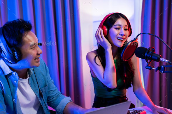 Asian audio DJ man and woman speaks into microphone to broadcasting.