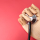 Closeup wooden hand holding stethoscope on a red background - PhotoDune Item for Sale