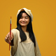 Asian girl wearing apron holding a paint brush isolate on yellow background. - PhotoDune Item for Sale