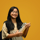 Smiling teenager schoolgirl with backpack holding books standing on yellow background. - PhotoDune Item for Sale