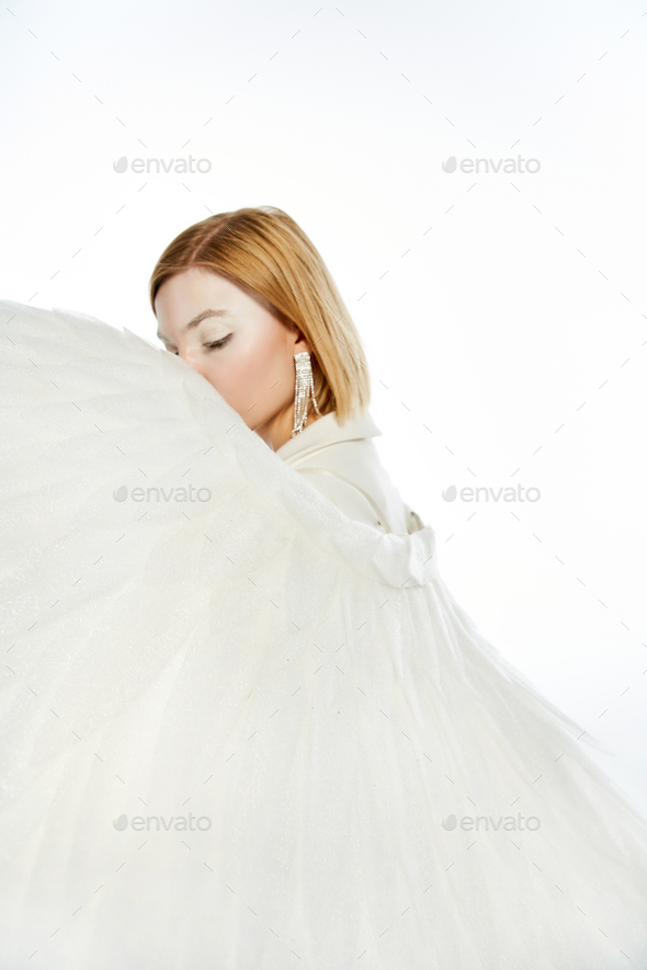 woman with angelic aura obscuring face with divine wings on white backdrop, purity and serene