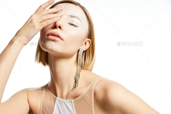 divine charm, woman with angelic face and enchanting makeup obscuring face with hand on white