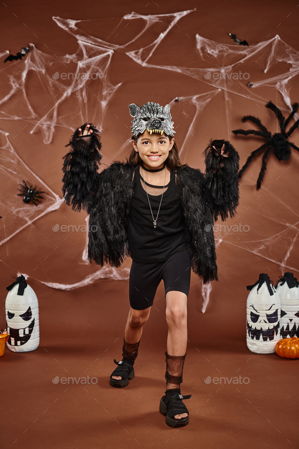 smiley preteen girl scaring and posing in faux fur attire with wolf mask, Halloween concept