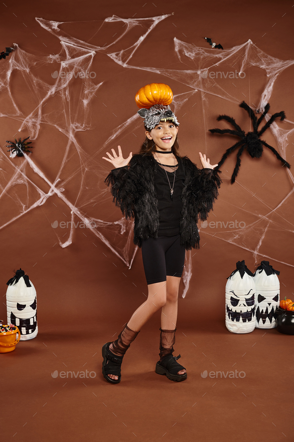 preteen girl holding pumpkin on her head with raised hands, brown