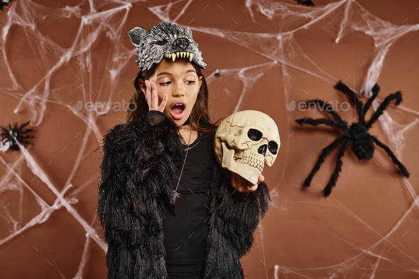 close up terrified preteen girl wearing wolf mask holds skull in her hands, Halloween concept
