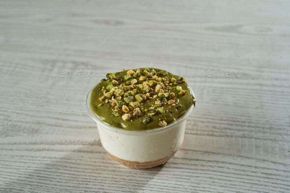 Cup of cheesecake with a green surface and crushed pistachios on it on a wooden background