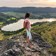 Young Woman Backpack Enjoys View To Green Landscape With Lake And Trees Standing On Rock At Sunset  - PhotoDune Item for Sale