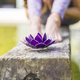 Aesthetic shot of a purple glass lotus on a tree trunk over the water. A praying woman is behind it. - PhotoDune Item for Sale