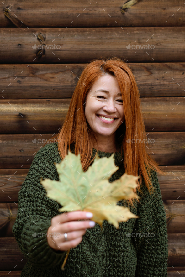 Autumn portrait young adult woman in sweater with maple leaf