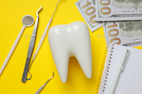 Dental tools, money, decorative tooth and notepad on yellow background, closeup