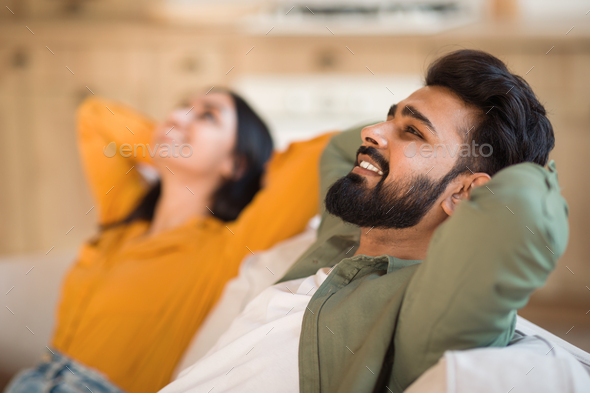 Time to relax. Calm indian couple resting, leaning back on sofa with hands behind head, selective