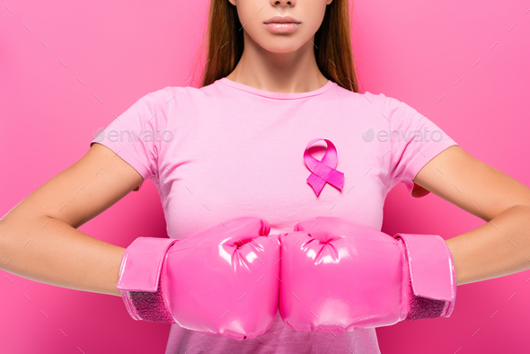Cropped view of young woman in pink boxing gloves and ribbon of breast cancer awareness on pink
