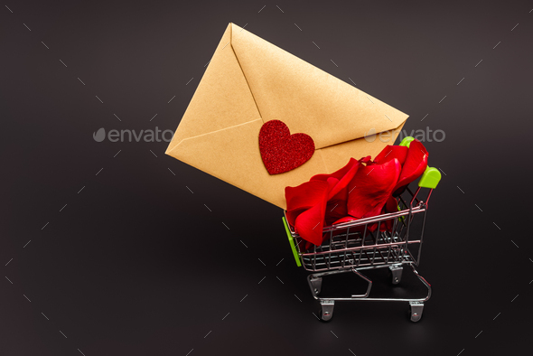 shopping cart with rose petals and envelope isolated on black