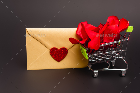 shopping cart with rose petals and envelope isolated on black