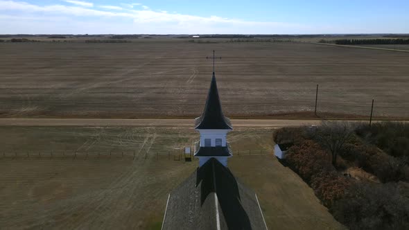 Backwards flying drone revealing secluded old church in Canadian countryside. 4k aerial footage of w alt