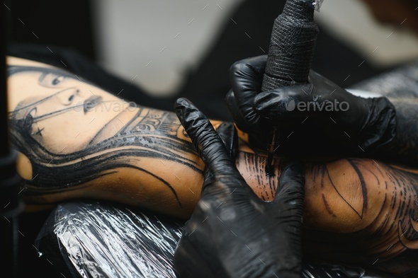 tattoo artist working at his studio tattooing sleeve on the arm of his male client.