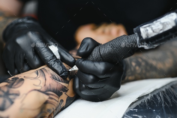 bearded tattoo artist working at his studio tattooing sleeve on the arm of his male client