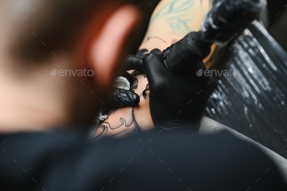 bearded tattoo artist working at his studio tattooing sleeve on the arm of his male client.