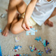 Puzzle piece in child hand. Little girl sits at home on the carpet and collects puzzles - PhotoDune Item for Sale
