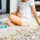 Little blonde girl sits at home on the carpet and collects puzzles. Focus on the puzzle pieces - PhotoDune Item for Sale
