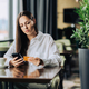 A serious young woman is sitting in a coffee shop and using her phone and credit card - PhotoDune Item for Sale