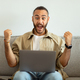 Super happy millennial man using laptop at home, celebrating success - PhotoDune Item for Sale