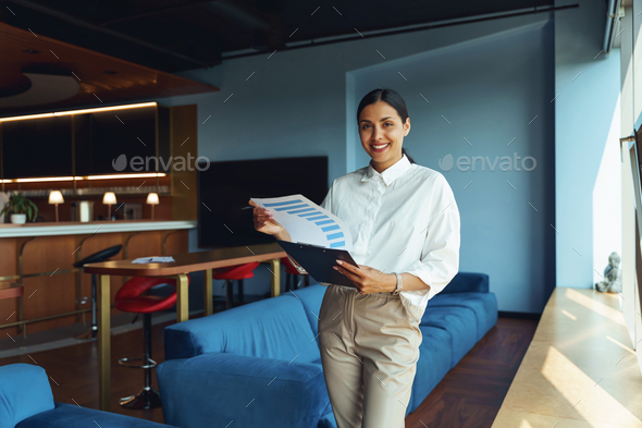 Woman analyst standing in office with financial statements documents and looking on camera  - Stock Photo - Images