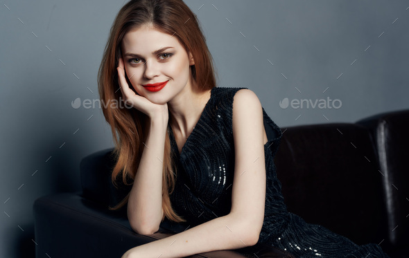 Pretty woman in black dress sits on luxury couch red lips