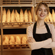 Young woman standing behind counter in artisan bakery and smiling - PhotoDune Item for Sale