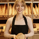 Smiling young woman holding fresh bread in artisan bakery - PhotoDune Item for Sale