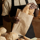 Young man putting fresh bread in paper bag serving customer in bakery - PhotoDune Item for Sale
