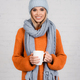 Young woman in knitted sweater, hat and scarf holding cup and smiling on white background - PhotoDune Item for Sale
