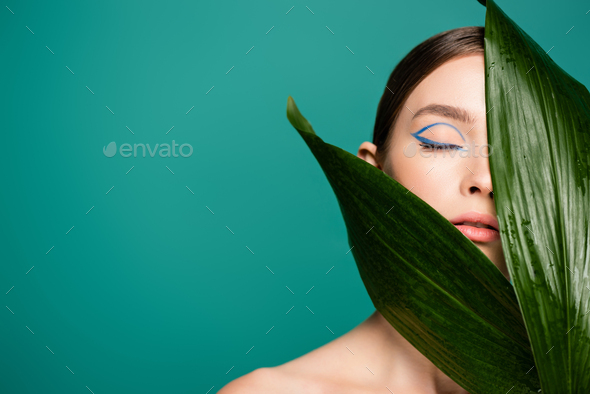 portrait of young woman obscuring face with glossy leaves isolated on green