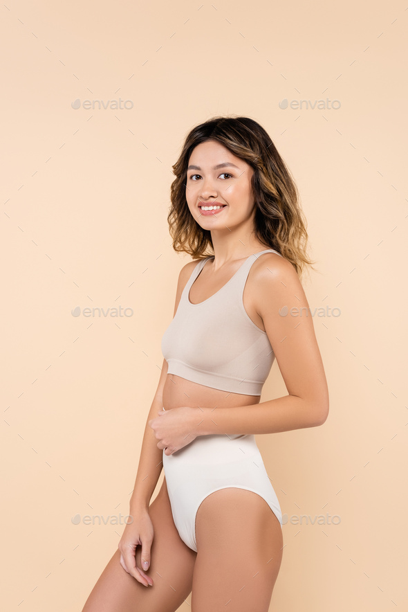 pleased asian woman in underwear smiling at camera isolated on beige Stock  Photo by LightFieldStudios